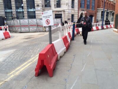 Londona. Ir gan fiziski norobežojumi, gan informatīvs plakāts, kas aicina gājējus neiet būvdarbu zonā.