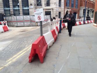 Londona. Ir gan fiziski norobežojumi, gan informatīvs plakāts, kas aicina gājējus neiet būvdarbu zonā.