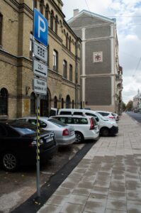 Pie tam stāvvietā novietotās automašīnas daļēji atrodas uz ietves.